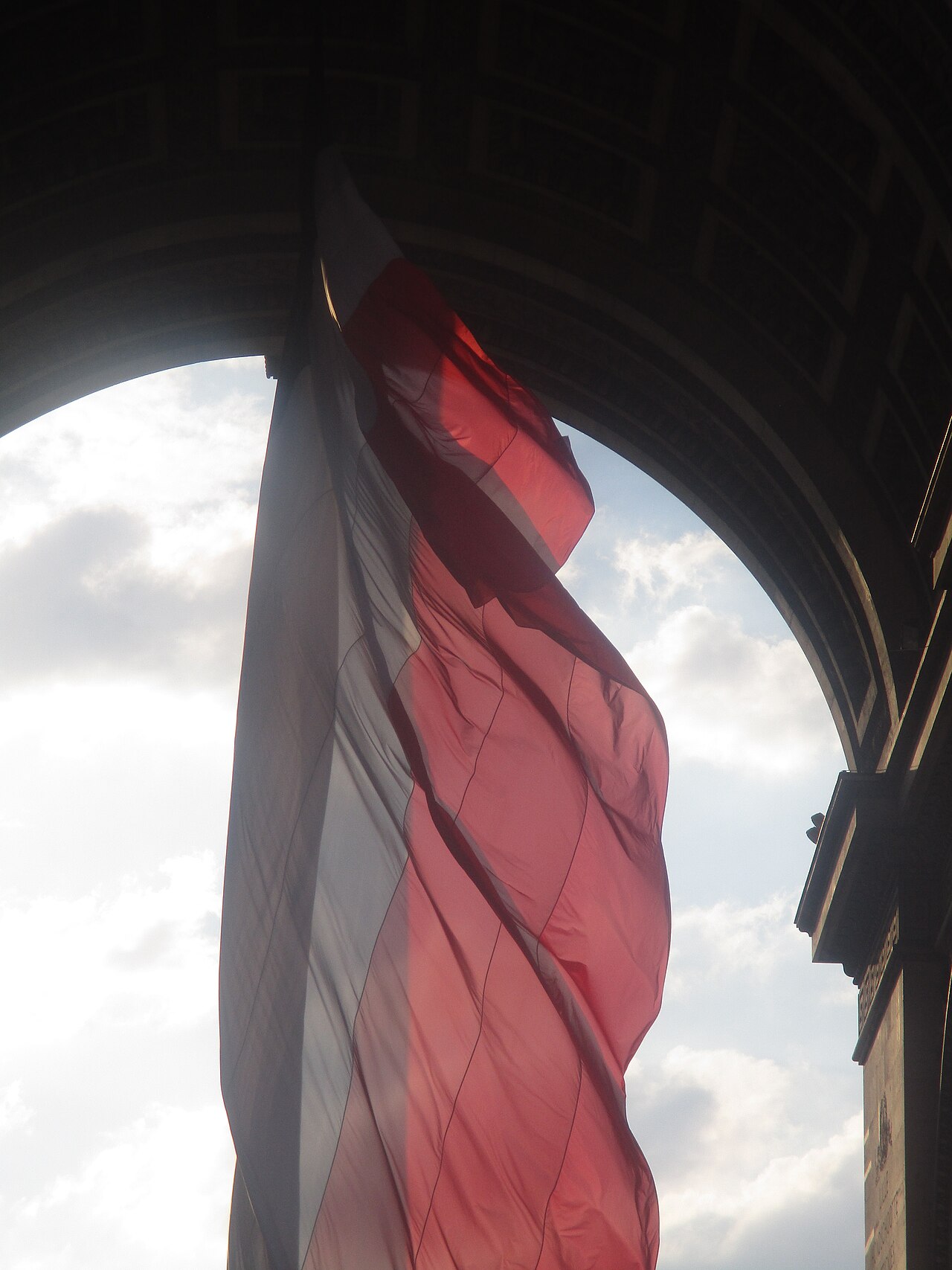 Immense drapeau tricolore bleu blanc rouge suspendu sous la voûte de l'Arc de Triomphe à Paris, emblème national de la République française